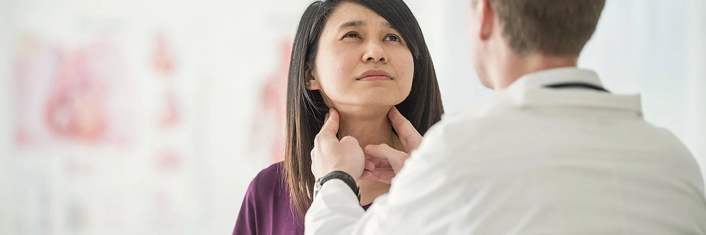Ein Arzt untersucht mit den Händen die Schilddrüse einer jungen Frau.