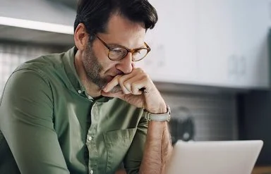 Ein Mann sitzt in einer Küche und schaut konzentriert auf seinen Laptop.
