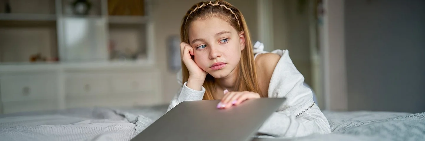Ein Mädchen schaut sehr traurig. Mit der rechten Hand stützt sie den Kopf ab, mit der linken klappt sie den Laptop zu.