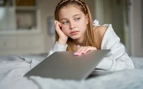 Ein Mädchen schaut sehr traurig. Mit der rechten Hand stützt sie den Kopf ab, mit der linken klappt sie den Laptop zu.