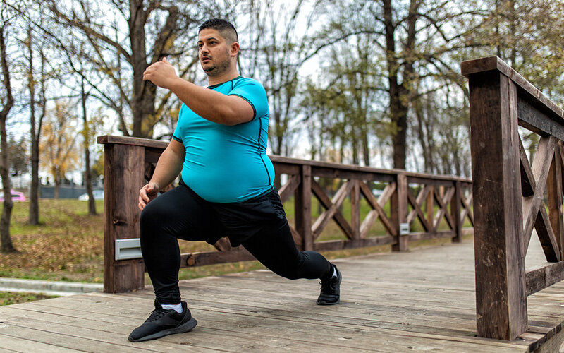 Ein Mann mit Übergewicht macht Sport in einem Park.
