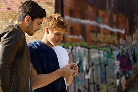 Zwei Männer auf der Straße, sie blicken gemeinsam auf ein Smartphone.