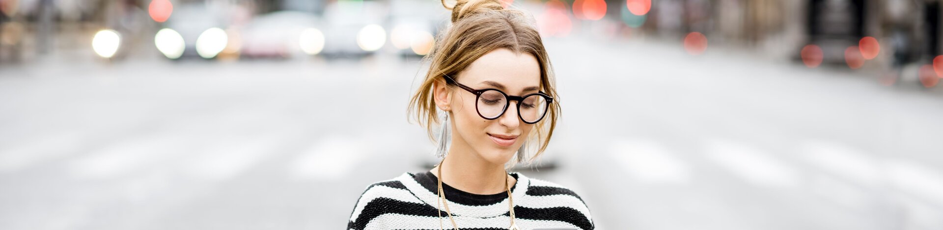 Junge Frau mit schwarzer Brille und Zebra-Pullover schaut auf ihr Handy.