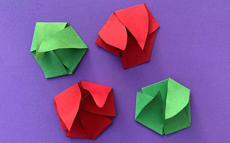 Vier zusammengefaltete Seerosen aus Tonpapier liegen auf einr violettblauen Fläche. Zwei Seerosen sind grün und zwei rot.