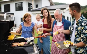 Eine Mehrgenerationenfamilie grillt im Garten umweltfreundlich mit Gas, Gemüse und Hähnchen.