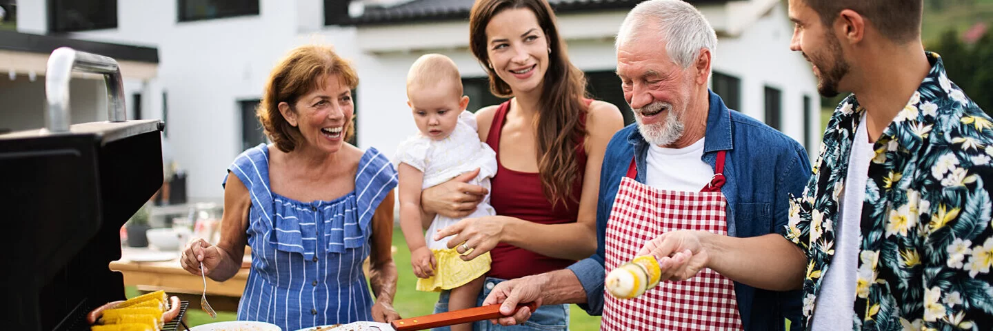 Eine Mehrgenerationenfamilie grillt im Garten umweltfreundlich mit Gas, Gemüse und Hähnchen.