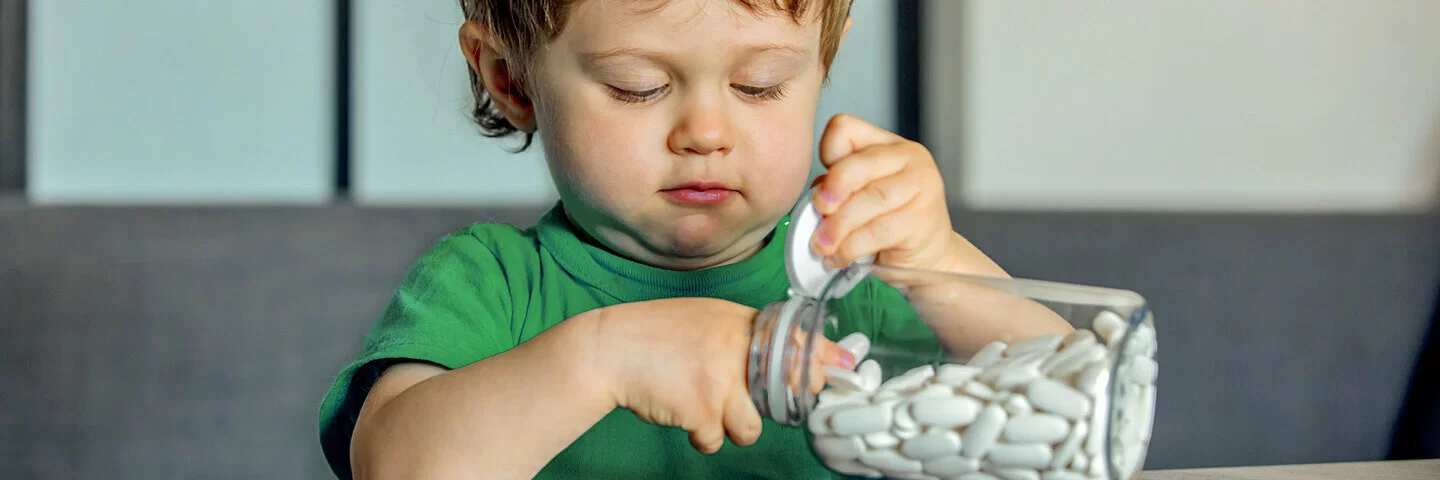 Ein kleines Kind greift in ein großes Fläschchen voller weißer Tabletten.