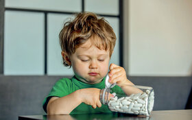Ein kleines Kind greift in ein großes Fläschchen voller weißer Tabletten.
