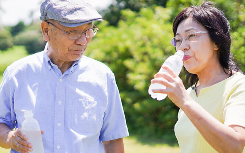 Ein älteres Paar trinkt im Park Wasser, um sich vor Überhitzung zu schützen.