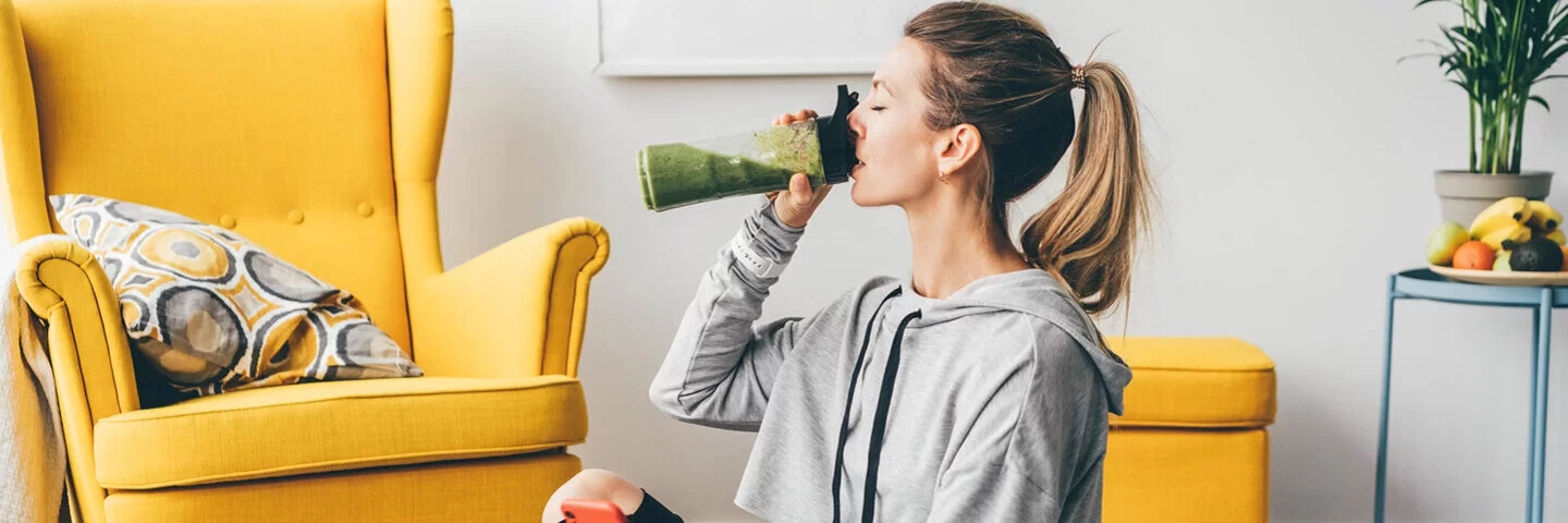 Eine junge Frau die Heilfasten betreibt, sitzt auf dem Boden und trinkt einen Smoothie.