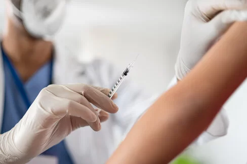 Eine Arzt ist kurz davor, einer Person eine Impfung in den Oberarm zu injizieren.