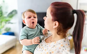 Ein Baby auf dem Arm der Mutter hat Keuchhusten und hustet stark.