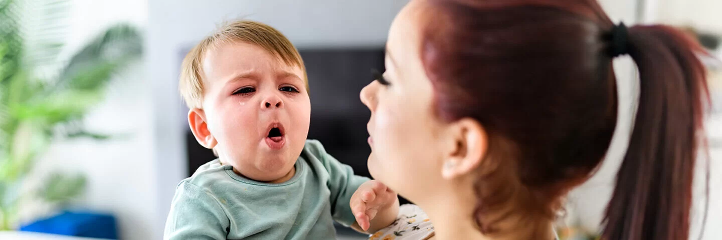 Ein Baby auf dem Arm der Mutter hat Keuchhusten und hustet stark.