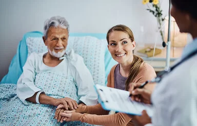 Ein älterer Patient liegt im Krankenhausbett und h�ält die Hand seiner Tochter. Die Tochter schaut zum Arzt.
