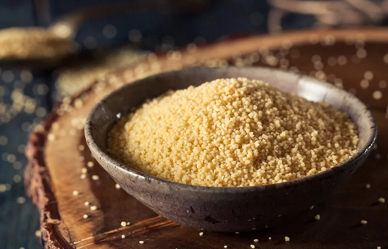 Eine Schüssel mit Couscous steht auf einem Holzbrett.