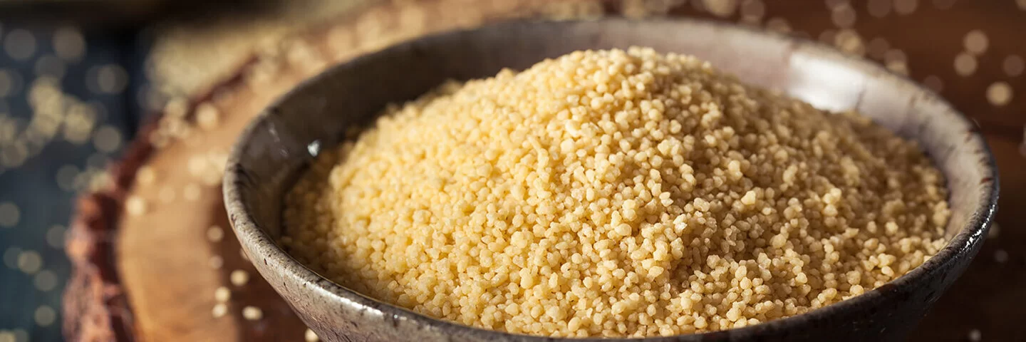 Eine Schüssel mit Couscous steht auf einem Holzbrett.