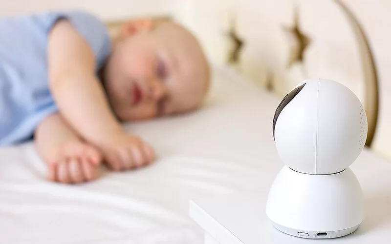 Ein Baby liegt im Bett und schläft. Auf dem Nachttisch steht ein Babyphone.