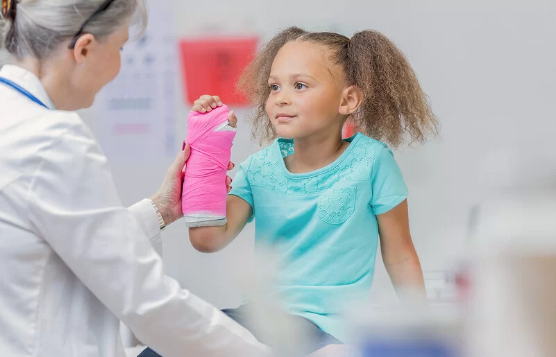 Ein kleines Mädchen mit einen Gipsverband am rechten Unterarm bei einer Untersuchung durch eine Ärztin.