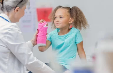 Ein kleines Mädchen mit einen Gipsverband am rechten Unterarm bei einer Untersuchung durch eine Ärztin.