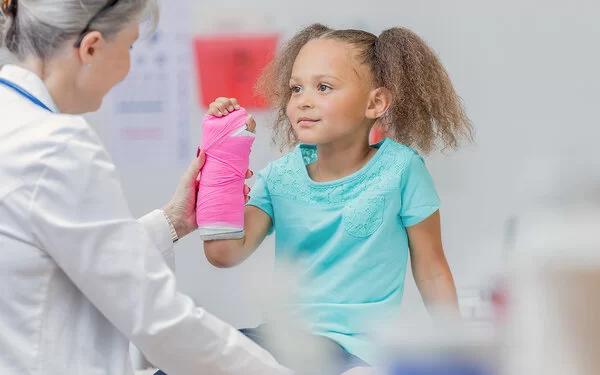 Ein kleines Mädchen mit einen Gipsverband am rechten Unterarm bei einer Untersuchung durch eine Ärztin.