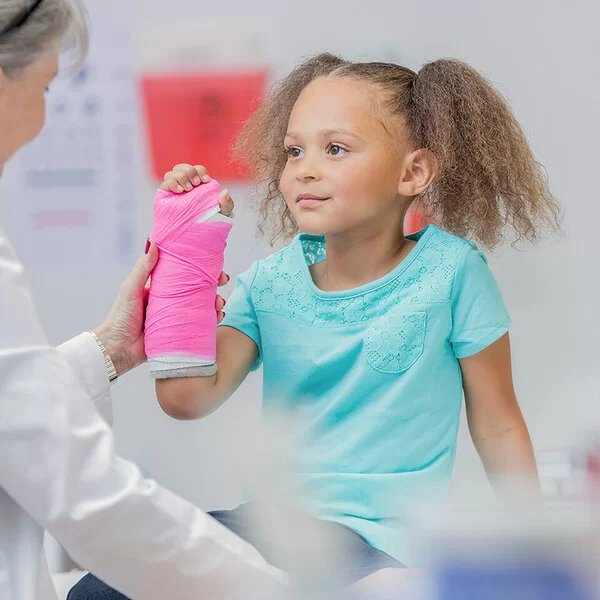 Ein kleines Mädchen mit einen Gipsverband am rechten Unterarm bei einer Untersuchung durch eine Ärztin.