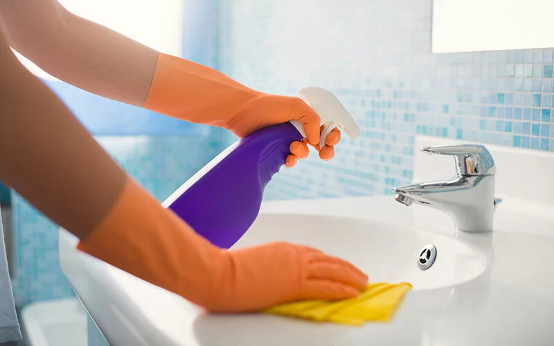 Eine Person reinigt das Badezimmer mit Reiniger und Handschuhen, um einen Befall mit Silberfischchen vorzubeugen.