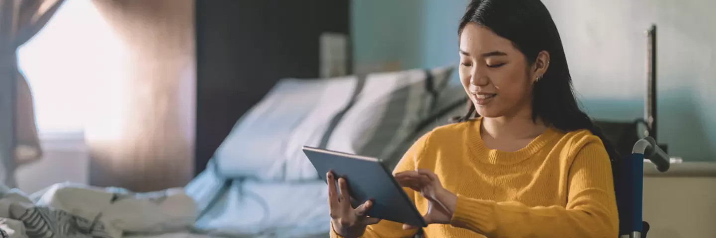 Eine junge Frau im Rollstuhl hält ein Tablet in der Hand.