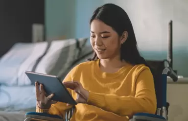 Eine junge Frau im Rollstuhl hält ein Tablet in der Hand.