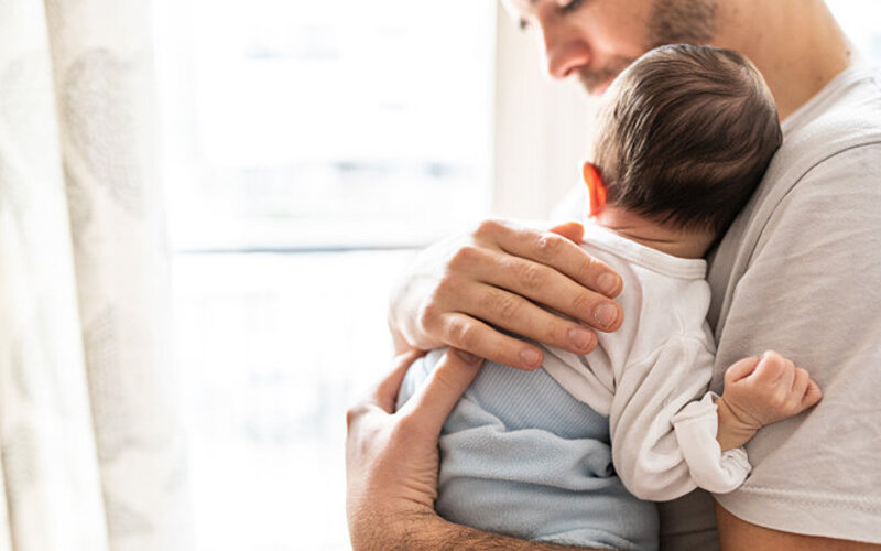 Ein Vater hält sein Baby mit Schlafregression auf dem Arm.