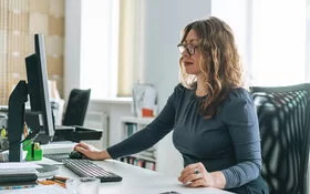 Eine Frau arbeitet am Schreibtisch und leidet unter Bewegungsmangel.