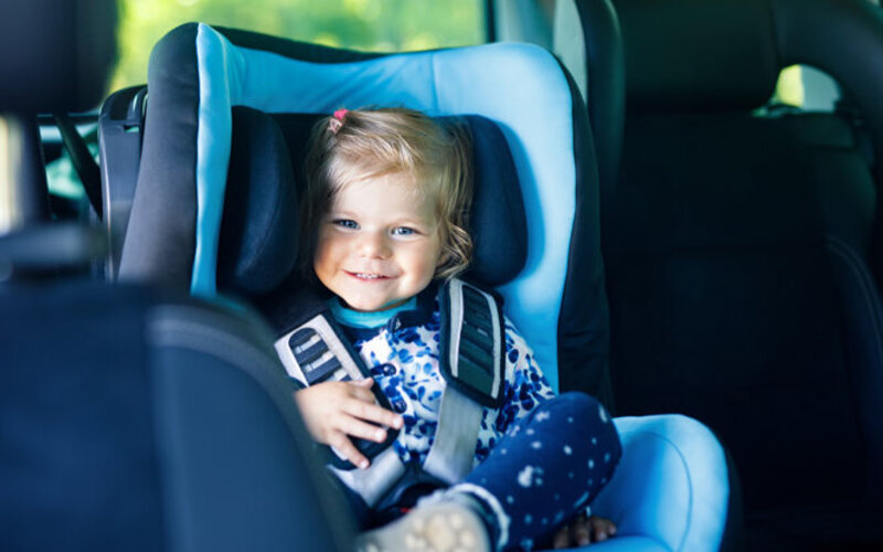 Kleines Mädchen sitzt gut geschützt vor einer Gehirnerschütterung im Kindersitz im Auto.