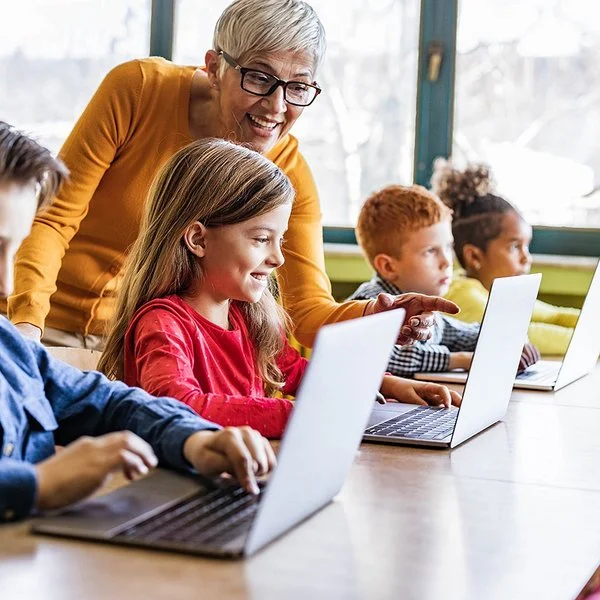 Eine Lehrerin unterrichtet Jungen und Mädchen im Grundschulalter an Laptops.