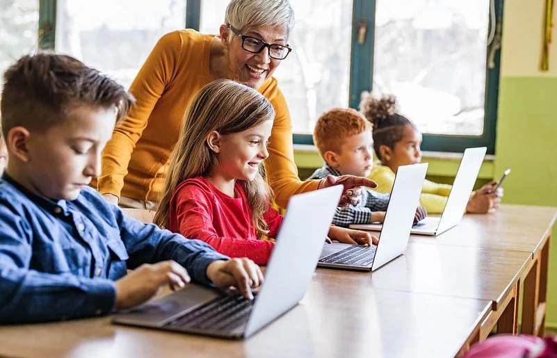 Eine Lehrerin unterrichtet Jungen und Mädchen im Grundschulalter an Laptops.