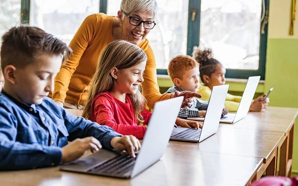Eine Lehrerin unterrichtet Jungen und Mädchen im Grundschulalter an Laptops.
