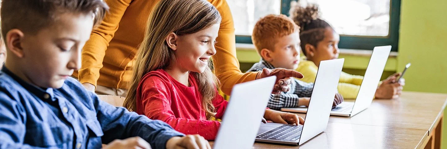 Eine Lehrerin unterrichtet Jungen und Mädchen im Grundschulalter an Laptops.