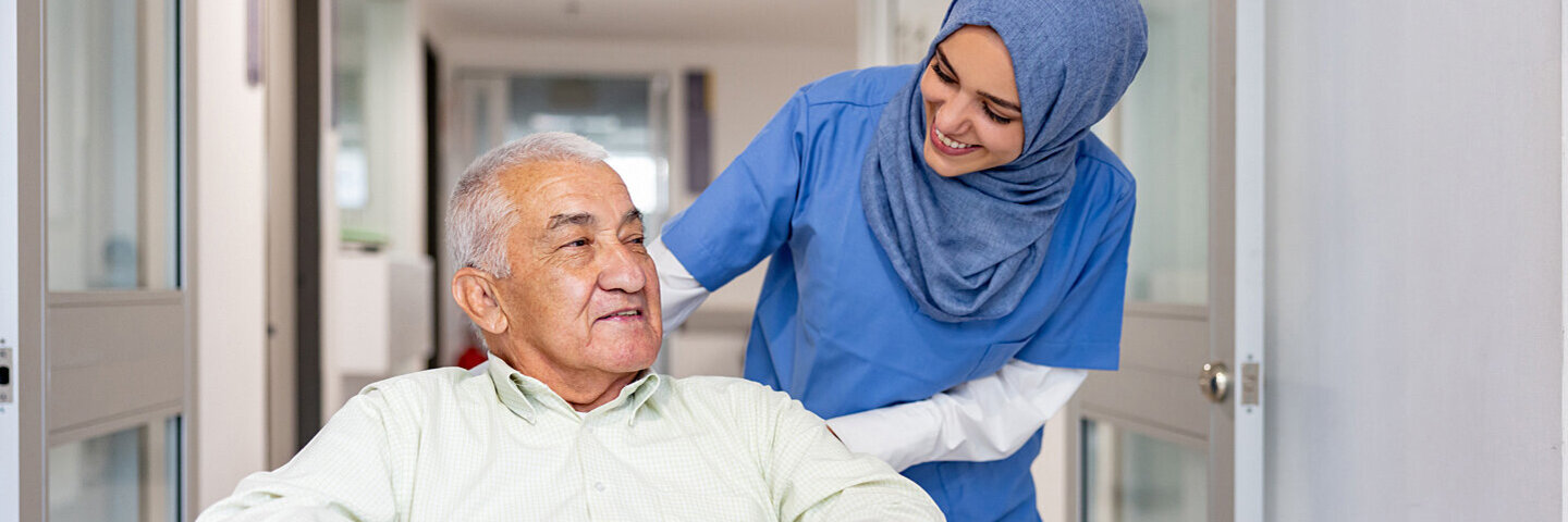 Krankenschwester schiebt ihren Patienten im Rollstuhl durch den Flur.
