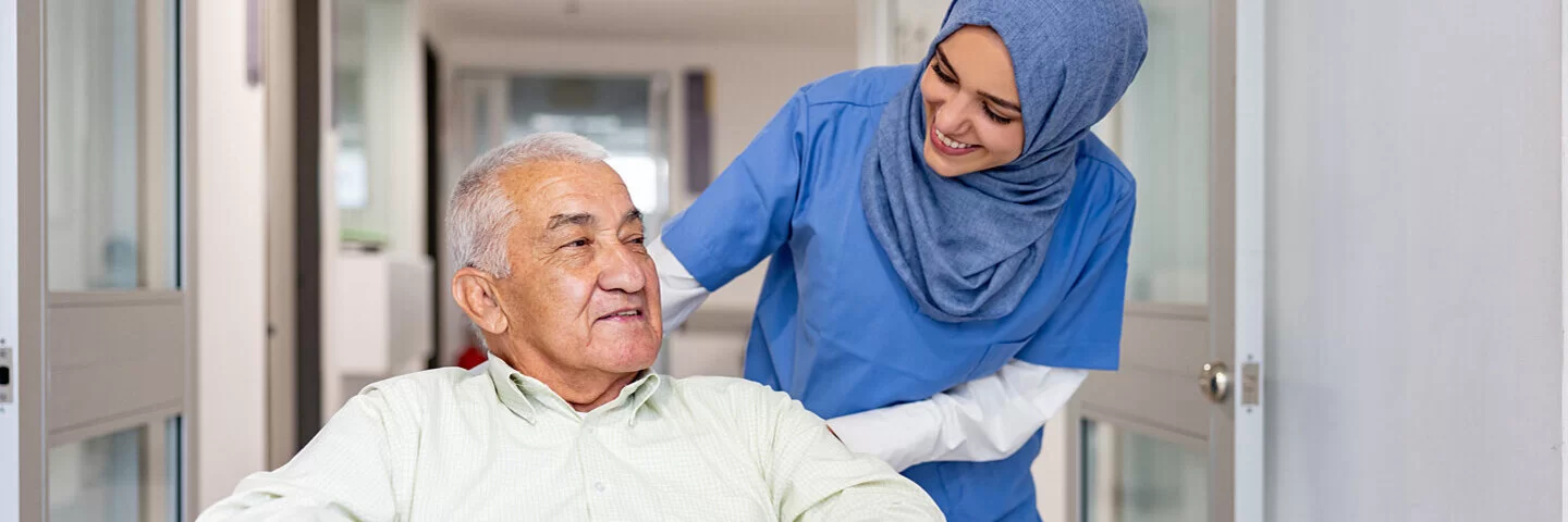 Krankenschwester schiebt ihren Patienten im Rollstuhl durch den Flur.