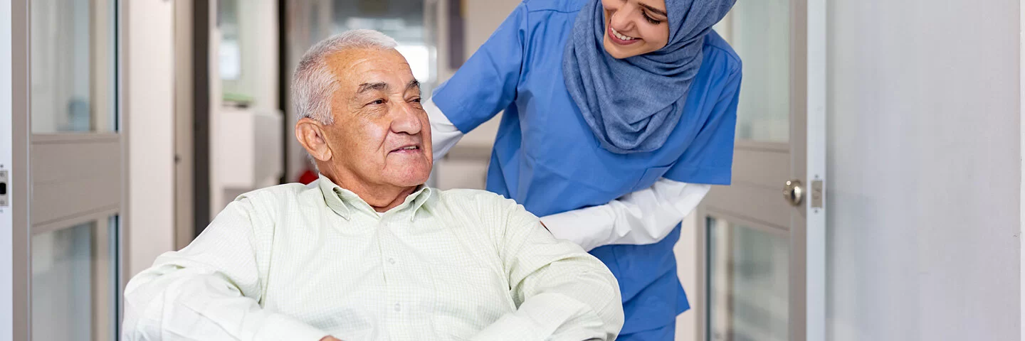 Krankenschwester schiebt ihren Patienten im Rollstuhl durch den Flur.