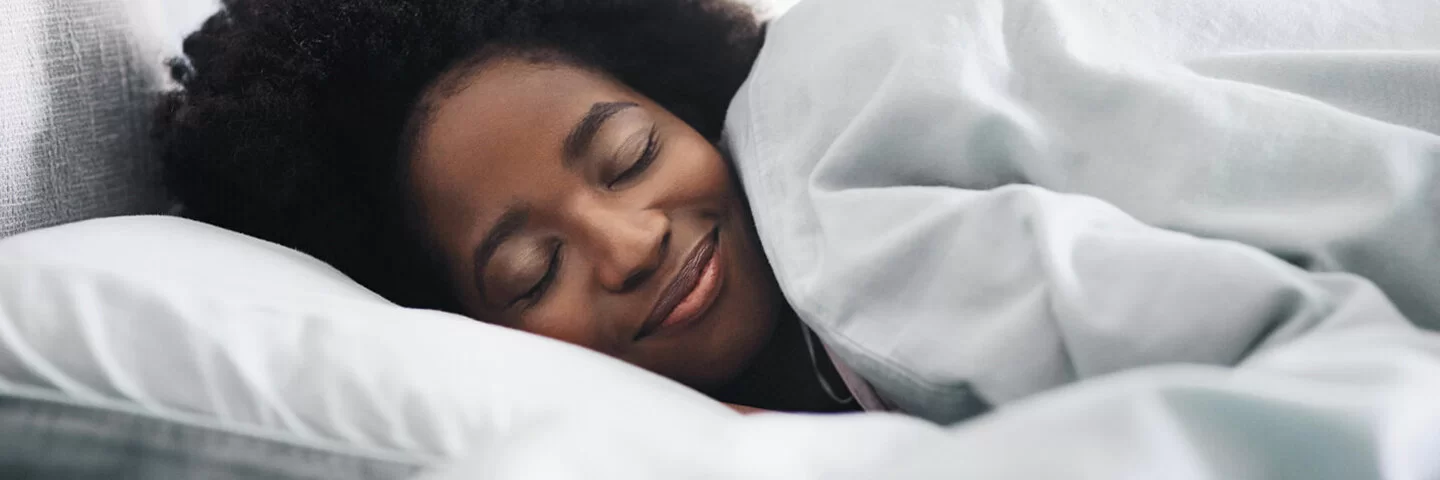 Eine junge Frau liegt mit geschlossenen Augen seitlich im Bett und lächelt.