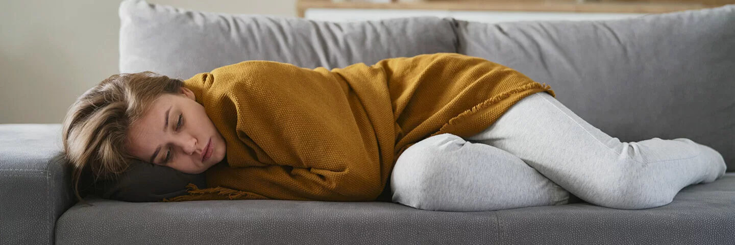 Eine junge Frau liegt erschöpft auf der Couch.