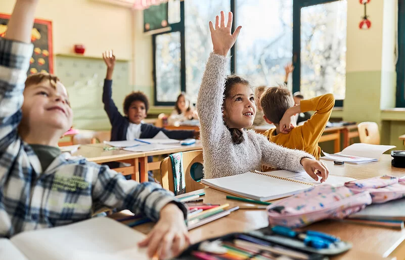 Grundschulkinder sitzen im Schulunterricht und melden sich.