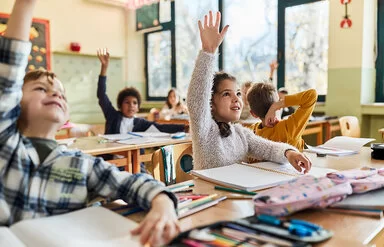 Grundschulkinder sitzen im Schulunterricht und melden sich.