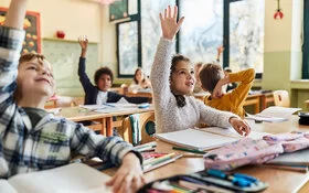Grundschulkinder sitzen im Schulunterricht und melden sich.