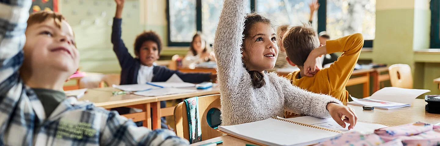 Grundschulkinder sitzen im Schulunterricht und melden sich.