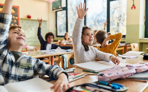 Grundschulkinder sitzen im Schulunterricht und melden sich.