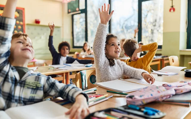 Grundschulkinder sitzen im Schulunterricht und melden sich.