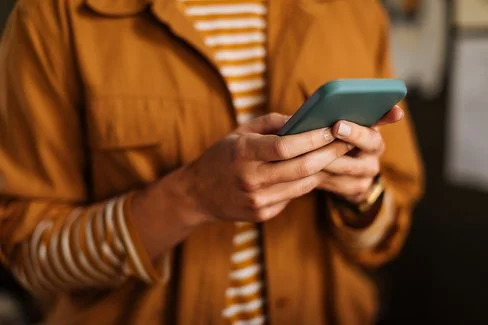 Eine nicht erkennbare Person hält ein Smartphone in den Händen und tippt mit den Daumen aufs Display.
