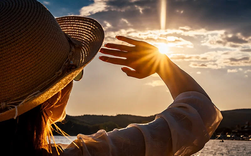 Eine junge Frau schützt am Strand ihr Gesicht mit ihrer Hand vor der tiefstehenden Sonne.