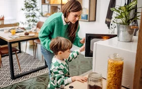Eine Mutter und ihr kleiner Sohn sind seitlich zu sehen. Sie öffnen die Tür einer Mikrowelle und schauen hinein.