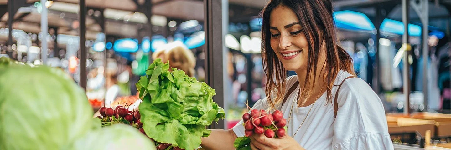 Eine Frau greift auf dem Markt nach frischen Radieschen.